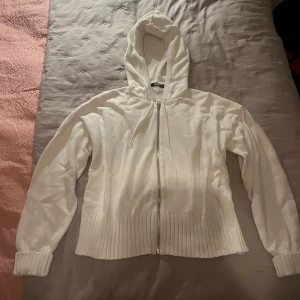 Vit stickad hoodie från BikBok - Vit stickad hoodie från BikBok i storlek XS. Tröjan har dragkedja framtill, huva med snörning och bred ribbad mudd vid ärmslut och nederkant. Perfekt för dig som gillar en enkel och clean look med mysig känsla.
