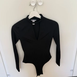 Svart långärmad bodysuit NLY One XS - Svart långärmad bodysuit från NLY One i storlek XS. Snygg v-ringning framtill och figurnära passform. Perfekt att styla med jeans eller kjol för en clean look. Materialet är stretchigt och bekvämt. Testad nån gång. 