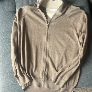 Beige cardigan jacka från MNG - Beige cardigan jacka från MNG med dragkedja framtill och ribbade muddar. Jackan har en stilren look med lång ärm och mjukt material, perfekt för lager-på-lager. Kragen är i kontrasterande ljusbeige och ger en snygg detalj till outfiten.  Nypris 380 säljer för 100kr