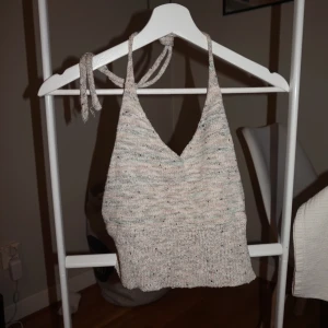 Stickad ljusgrå croppad linnetopp - Supersöt stickad linnetopp i ljusgrå toner med diskreta inslag av pastell. Toppen har smala knytband i nacken och en croppad passform. Perfekt för varma dagar eller lager på lager-stil.