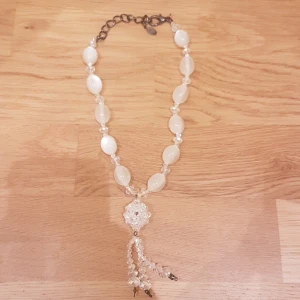 Vitt pärlhalsband med kristalldetalj - Unikt halsband med vita ovala pärlor och små glittrande kristaller. Hängsmycke i form av en blomma med tre hängande pärlsträngar. Perfekt för dig som gillar statement-smycken med elegant vibe. PRIS KAN DISKUTERAS!