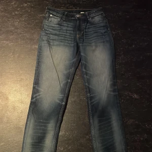 Blå tapered jeans från H&M - Snygga blå jeans från H&M med relaxed fit och justerbar midja. Jeansen har tapered ben, klassisk femficksdesign och coola slitningar för en trendig look. Perfekta för dig som gillar en avslappnad men ändå stilren vibe.