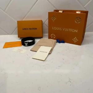 LV svart armband  - Snyggt svart armband från LV i äkta skinn med klassiskt LV-spänne i silverfärg. Armbandet har den ikoniska monogramdesignen och levereras med originalförpackning, dustbag och certifikat. Perfekt accessoar för att lyfta din outfit.