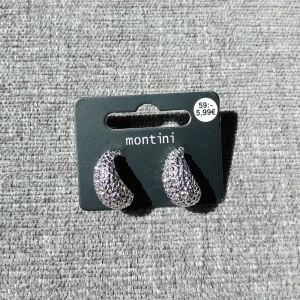 Glittriga silvriga örhängen Montini - Säljer ett par chunky silvriga örhängen från Montini med glittrig yta och cool struktur. De är halvbågsformade och riktigt statement, perfekta för att lyfta vilken outfit som helst. Snygga och trendiga örhängen för dig som gillar att sticka ut.