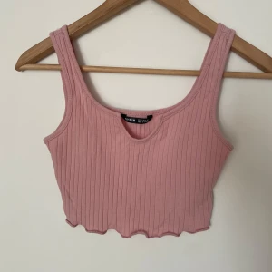 Rosa ribbad croppad linnetopp SHEIN - Supersöt ljusrosa croppad linnetopp från SHEIN med breda axelband och ribbad tyg. Toppen har en gullig vågig kant detalj nertill och en snygg, djupare rundad ringning framtill🩷