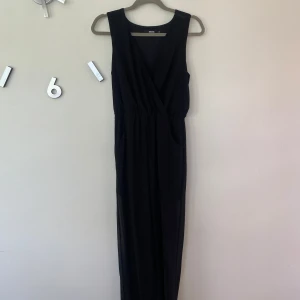 Svart Byxdress / Jumpsuit från Bik Bok XS - Svart byxdress från Bik Bok i storlek XS. Den är ärmlös med omlott-v-ringning och har resår i midjan för en snygg passform. Tillverkad i ett tunt, lätt och något transparent material som ger ett luftigt intryck. Använd fåtal gånger.