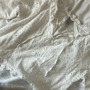 Vit broderad blus från Lindex XS/S - Superfin vit blus från Lindex i bomull med broderade detaljer och hålmönster. Blusen har långa ärmar, v-ringning med knyt och volangkant vid halsen. Perfekt för vår och sommar när du vill ha en luftig och söt look.
