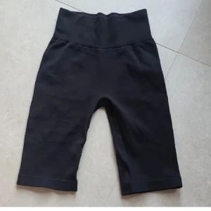 Svarta ribbade tränings-shorts XS/S - Svarta, ribbade shorts från Sloggi med hög midja och tight passform. Tillverkade i ett stretchigt material (96% polyamid, 4% elastan) som sitter skönt och följsamt. Perfekta för träning eller chill. Diskret logga baktill i midjan.