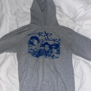 Grå hoodie Mount Rap More tryck - Snygg grå hoodie med blått Mount Rap More-tryck framtill. Tröjan har huva med snörning och en stor magficka. Mjuk och skön, passar till chill eller när du vill sticka ut lite extra.