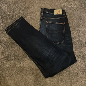 Mörkblå jeans från Nudie Jeans - Snygga mörkblå jeans från Nudie Jeans med klassisk femficksdesign och orange kontrastsömmar. Jeansen har raka ben och är tillverkade i slitstarkt denimtyg. Hör av er vid funderingar 
