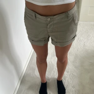 Beige shorts från Milk Atelier - Snygga beige shorts från Milk Atelier med klassisk passform och uppvikta benslut. De har fickor både fram och bak samt bälteshällor. Perfekta för varma dagar och lätta att matcha med allt. Tillverkade i mjuk bomull för en skön känsla.