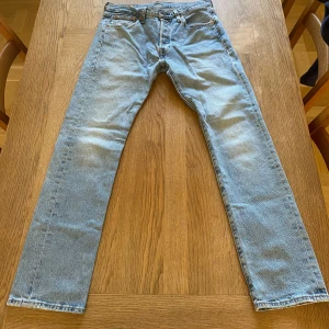 Levi's 501 ljusblå jeans W30 L30 - Klassiska Levi's 501 jeans i ljusblått med raka ben och normal passform. Jeansen har fem fickor, knappgylf och den ikoniska läderpatchen bak i midjan.  Något urtvättade på framsidan