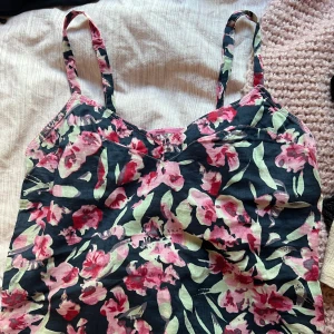 Blommig linnetopp med smala axelband - Snygg linnetopp med blommigt mönster i rosa, rött och grönt på mörk botten o justerbara band ifrån H&M. 