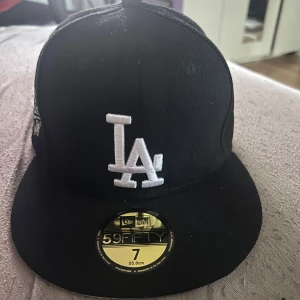 Svart LA Dodgers keps New Era 59FIFTY - Snygg svart LA Dodgers keps från New Era 59FIFTY med broderad LA-logga framtill och 1988 World Series-märke på sidan. Klassisk flat peak och MLB-logga bak. Perfekt för dig som gillar streetstyle och sportig vibe.