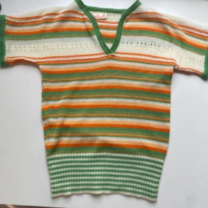 Randig stickad tröja från Romana - Retro stickad tröja från Romana i storlek S med färgglada ränder i grönt, orange och vitt. Tröjan har korta ärmar, v-ringning och ribbad nederkant. Perfekt för dig som gillar vintage vibes och unika plagg med coola färgkombinationer.