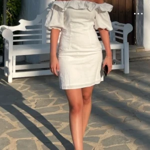 Trendig Vit offshoulder kortklänning - Superfin vit kortklänning med offshoulder och volang upptill. Klänningen har puffiga korta ärmar. 