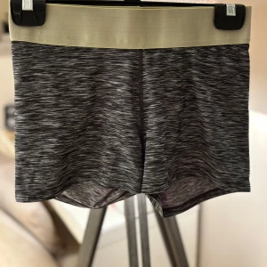 Gråmelerade träningstights-shorts - Snygga gråmelerade shorts med bred beige resår i midjan. De är stretchiga och sitter tight, perfekta för träning eller chill. Materialet är mjukt och följsamt, vilket gör dem riktigt bekväma att ha på sig.