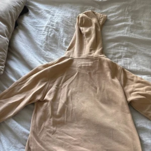Beige hoodie från Abercrombie & Fitch - Säljer en beige hoodie från Abercrombie & Fitch med klassisk huva och magficka. Tröjan har lång ärm och en liten vit logga broderad på bröstet. Perfekt för chill dagar och enkel att matcha med jeans eller mjukisbyxor. Lite skrynklig, STORLEK 152 11/12