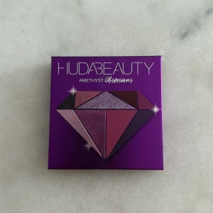 Huda Beauty Amethyst Obsessions palett - Säljer en Huda Beauty Amethyst Obsessions ögonskuggspalett med 9 nyanser i lila, rosa och vinröda toner. Paletten innehåller både matta och skimriga skuggor, perfekt för kreativa och färgstarka ögonlooks. Kompakt format med spegel i locket.