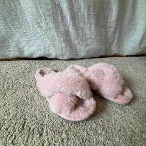 Fluffiga rosa sandaler (SMÅ I STORLEKEN) - Supermjuka och fluffiga sandaler i ljusrosa pälsimitation från Shoes. De har korslagda band över foten och öppen tå, perfekt för att chilla hemma eller mysa runt i. Sulan är platt och bekväm. Storlek 37.