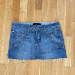 Blå jeanskjol från Pulz med fransad kant - Snygg blå jeanskjol från Pulz med fransad nederkant och coola fickdetaljer både fram och bak. 