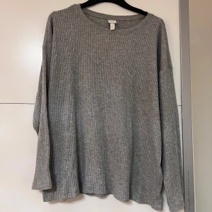 Grå ribbad långärmad tröja - Mysig grå långärmad tröja med ribbat mönster. Tröjan har en loose passform och rund halsringning, tillverkad i mjuk bomullsblandning.