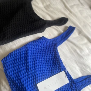 Blå och svart linnetopp från Amisu - Två ribbade linnetoppar från Amisu, en i klarblått och en i svart. Båda har en strukturerad, vågig yta och breda axelband. Båda för 150 o 1 för 80