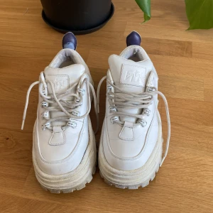 Chunky vita sneakers från Eytys - Säljer ett par chunky vita sneakers från Eytys med kraftig plattformssula och snörning. Skorna är tillverkade i skinn med foder i kalvskinn och har en robust gummisula. Ikonisk Eytys-logga på plösen och lila detalj bak på hälen.