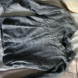 Grå stickad tröja från Amisu XS - Mysig grå stickad tröja från Amisu i storlek XS. Tröjan har v-ringad halsringning, ribbade muddar och är långärmad. Perfekt för lager-på-lager och chill dagar. Enkel att matcha med jeans eller kjol.