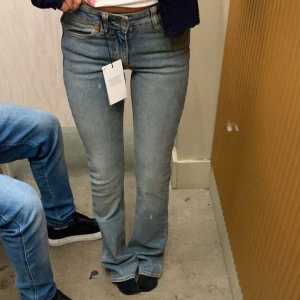 Blå bootcut jeans från junkyard - Snygga ljusblå bootcut jeans från junk yard med klassiska fem fickor och coola detaljer på bakfickorna. Jeansen har normal passform och är tillverkade i mjukt bomullsjeansmaterial. Perfekta för en avslappnad och trendig look. Original pris 699kr. Inga stora tecken på användning 