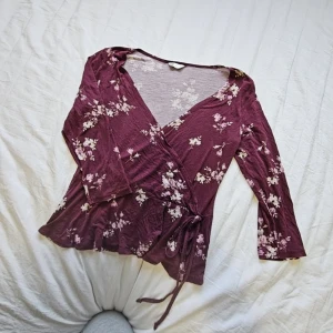 Omlott topp - En riktigt fin vinröd omlott topp med trekvartsärm och knytning. Blommig och perfekt till alla tillfällen, storlek S från cubus. Använd fåtal gånger! 💞