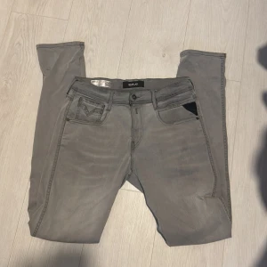 Replay Anbass Hyperflex grå jeans - Snygga grå Replay Hyperflex jeans med klassisk femficksdesign och diskreta sömmar på bakfickorna. Jeansen har en smal passform och är tillverkade i stretchigt material för extra komfort. Perfekta för dig som gillar stilrena och moderna jeans. Storlek 30/32