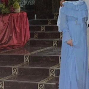 Ljusblå långklänning med volang - Superfin ljusblå långklänning med volangdetaljer upptill och långa ärmar. Klänningen har en elegant och flowy känsla, perfekt för dig som vill sticka ut med en romantisk look. Snyggt bälte i midjan för extra form. bälten är lite trasig där bak men går att fixa passar M lch L