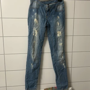 Blå slitna jeans med raka ben - Säljer ett par blå jeans med slitna detaljer och raka ben. Jeansen har klassisk femficksdesign, normal midja och dragkedja med knapp. Perfekta för en avslappnad och trendig look.