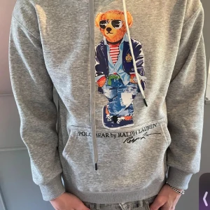 Grå hoodie Polo Bear Ralph Lauren - Säljer en grå hoodie från Ralph Lauren med ikoniskt Polo Bear-tryck framtill. Tröjan är knappt använd. Skick 10/10. Säljs pga den är lite liten