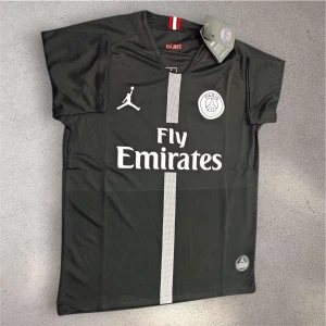 Svart PSG fotbollströja Jordan x Fly Emirates - Svart PSG fotbollströja med vit vertikal rand och tryckta loggor från Jordan och Paris Saint-Germain. Fly Emirates sponsortryck på bröstet. Kortärmad modell i lätt och ventilerande material, perfekt för match eller träning.
