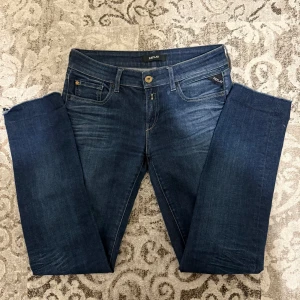 Replay mörkblå jeans med råa benslut - Snygga mörkblå jeans från Replay med klassisk femficksdesign och råa, fransiga benslut. Jeansen har guldfärgade detaljer, diskret Replay-logga och är tillverkade i stretchig denim för skön passform. Perfekta för dig som gillar en stilren men avslappnad look.