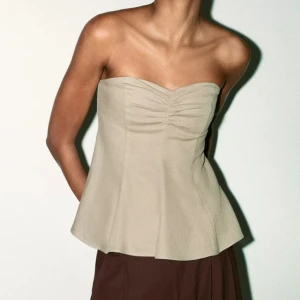 Beige bandeau tubtopp med rynk - Supersnygg beige bandeau tubtopp med lätt utsvängd passform och rynkdetalj framtill. Toppen är axelbandslös och har en stilren, minimalistisk look som passar perfekt till jeans eller kjol. Materialet känns svalt och mjukt mot huden. Helt ny med prislapp kvar