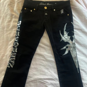 Svarta Blue Queen jeans  - Svarta jeans från Blue Queen med paljetter, jättelågmidjade och bootcut. Midjemåttet är 38cm rakt över och innerbenslängden är 84cm
