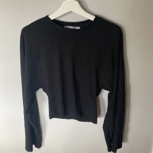 Svart långärmad topp - Svart långärmad topp från Lager 157 i storlek XS. Modellen är croppad med en tight passform och har vida ärmar som ger en cool och modern look. Tillverkad i mjukt bomullsmaterial som känns skönt mot huden. Perfekt att styla med jeans.