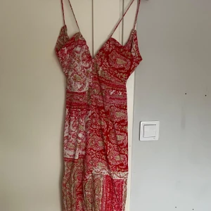 Röd och vit långklänning med mönster - Supersöt långklänning med tunna axelband och knytning i ryggen. Klänningen har ett färgstarkt rött och vitt paisleymönster med inslag av grönt. Lätt och luftig, perfekt för varma dagar. Sitter snyggt med v-ringning och smickrande passform. Från Zara