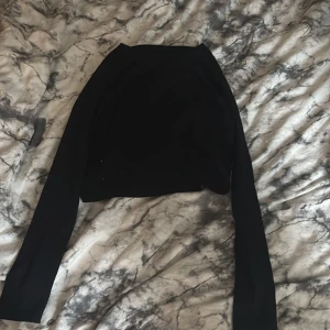 Svart croppad tröja från 157 - Svart croppad långärmad tröja från 157. Enkel och stilren design med rund halsringning. Tillverkad i mjuk bomull med lite stretch för en skön passform. Perfekt till jeans eller kjol för en clean look.