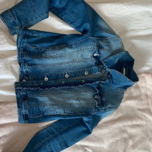 Jeanjacka med ruffles - Snygg blå jeansjacka från Name It i storlek 164. Klassisk modell med knappar framtill, krage och långa ärmar. Använd väldigt få gånger💕