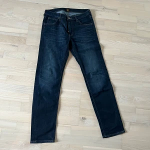 Mörkblå Lee jeans straight fit - Snygga mörkblå jeans från Lee med klassisk femficksdesign och raka ben. Jeansen har kontrastsömmar och Lee-logga på bakfickan. Perfekta för dig som gillar en tidlös och clean look. Materialet är slitstarkt denim i bomull.
