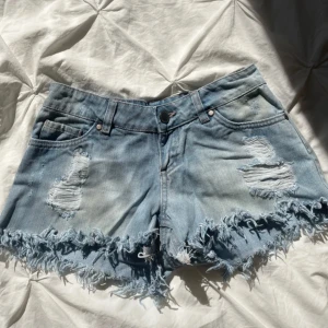 Jeansshorts - Lågmidjade jeansshorts med slitningar, inga tecken på användning. MIDJEMÅTT: 33.5 cm, MIDJEHÖJD: 12 cm