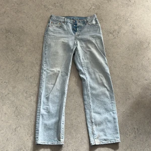 Levi's 501 ljusblå jeans W27 L32 - Säljer ett par klassiska Levi's 501 jeans i ljusblå tvätt. De har raka ben, mid waist och knäppning med knappar. Jeansen är i 99% bomull och har den ikoniska läderpatchen bak samt röda Levi's-taggen på fickan.