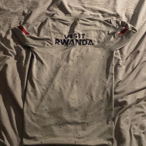 PSG x Jordan långärmad fotbollströja  - Snygg långärmad PSG fotbollströja i ljusgrått med mörkblå och röda detaljer. Tröjan har prickigt mönster, halv dragkedja och Paris Saint-Germain-logga på bröstet. Tillverkad i ett lätt och sportigt material, perfekt för träning eller match.