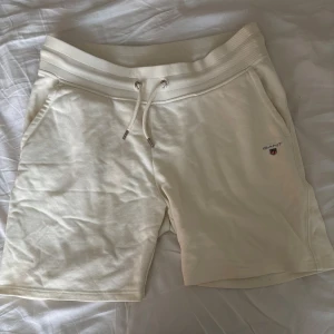 Vita shorts från GANT, Strlk M-L - Snygga vita shorts från GANT med bekväm resårmidja och snörning framtill. Mjukt bomullsmaterial, två fickor fram och en bakficka. Perfekta för sommardagar och chill vibes. Liten Gant-logga broderad på ena benet. Nypris är 1100kr! 