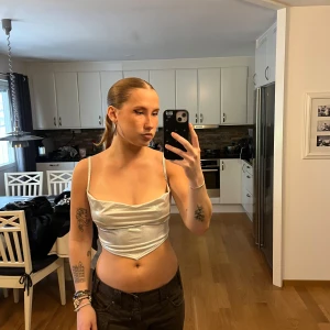 Silvrig croppad linnetopp från ASOS - Säljer en glansig silvrig linnetopp med smala axelband och draperad framsida. Toppen är croppad och har en spetsig nederkant framtill, perfekt för att sticka ut. Materialet är syntet och ger en cool metallic-look. Storlek 10 (S)