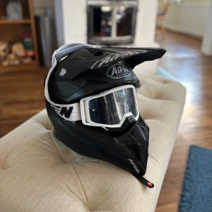 Svart crosshjälm Airoh Raven glasögon - Säljer en svart crosshjälm från Airoh med cool design och skärm framtill. Hjälmen har matchande vita Raven crossglasögon med bred resårrem. Perfekt för motocross eller moped. Hjälmen är lätt och har ventiler för bra luftflöde. Nypris 1349, lägg bud!